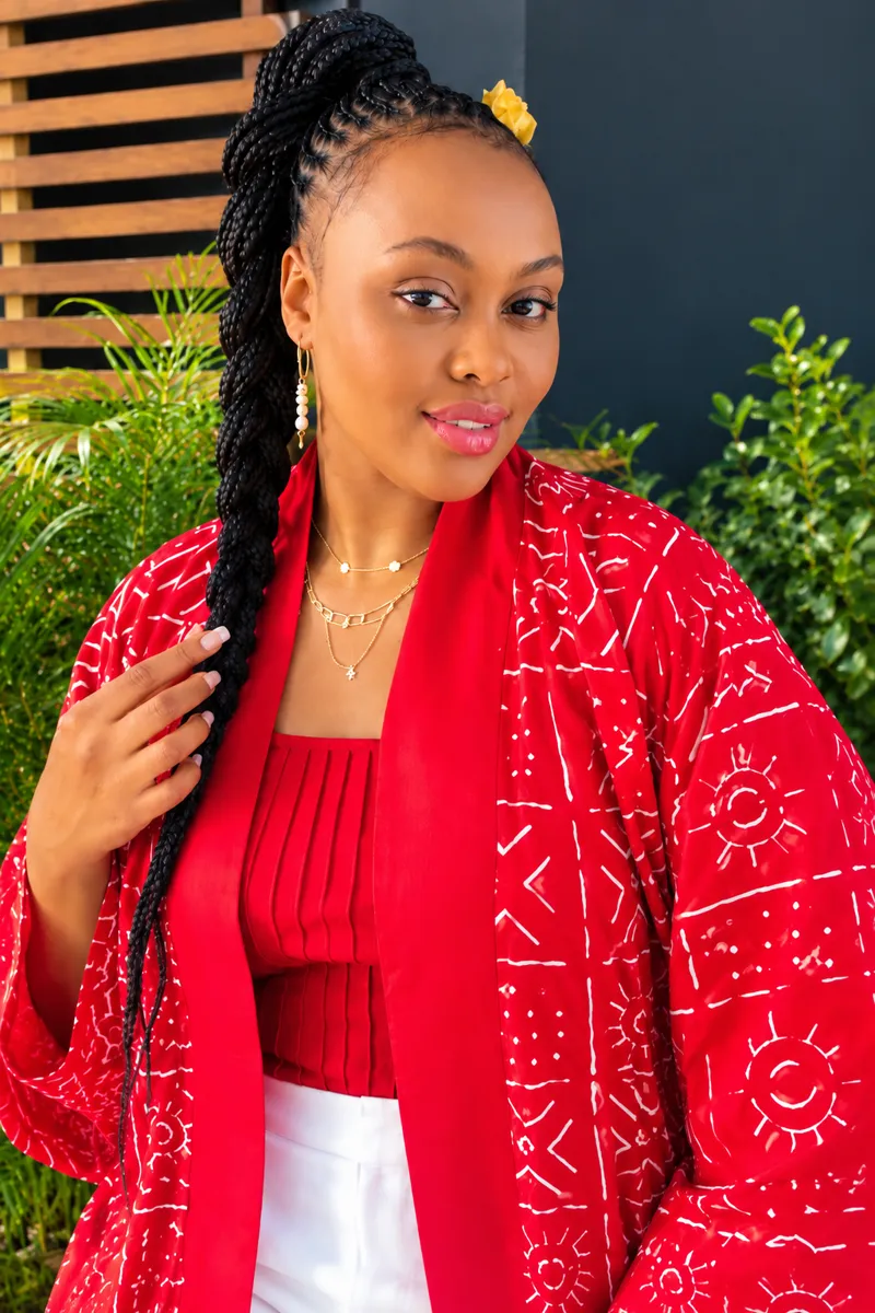 Customer in a red and white print kimono over a red top, with a braided updo and yellow flower, in a leafy garden
