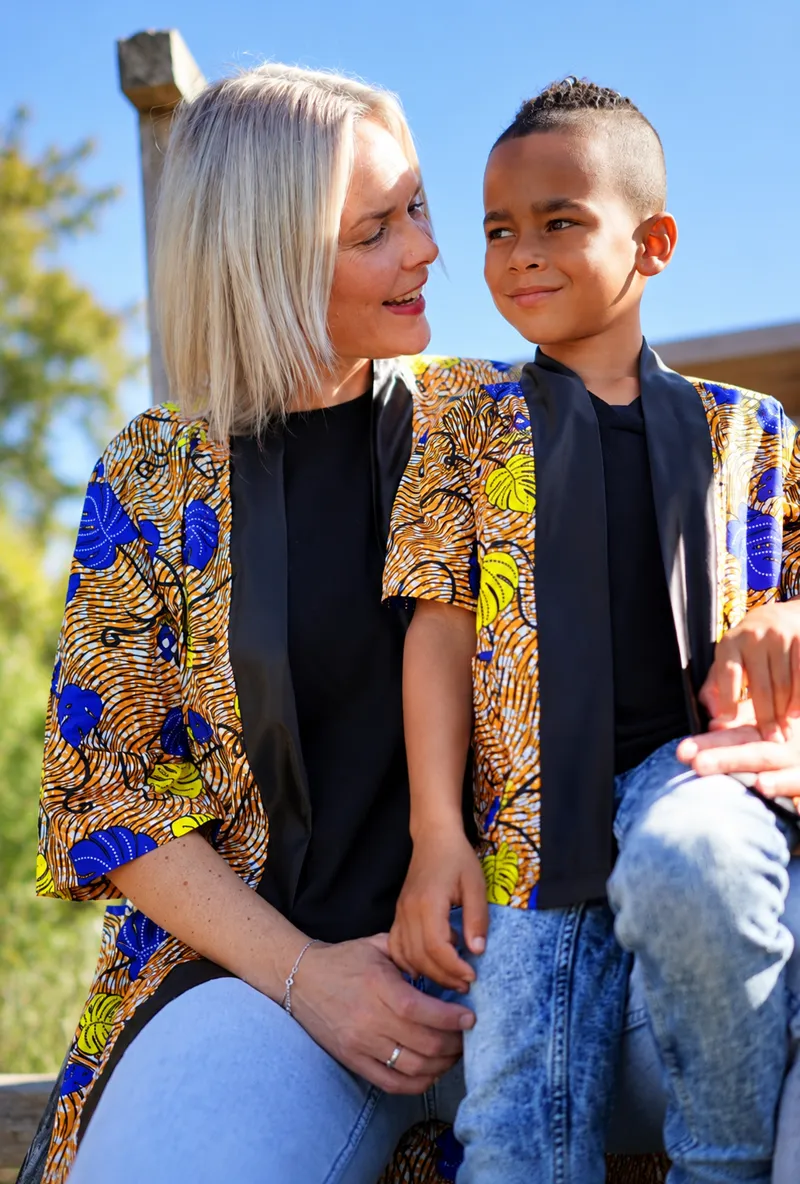 A customer and a young boy in matching orange and blue print jackets, sitting side by side under a clear blue sky